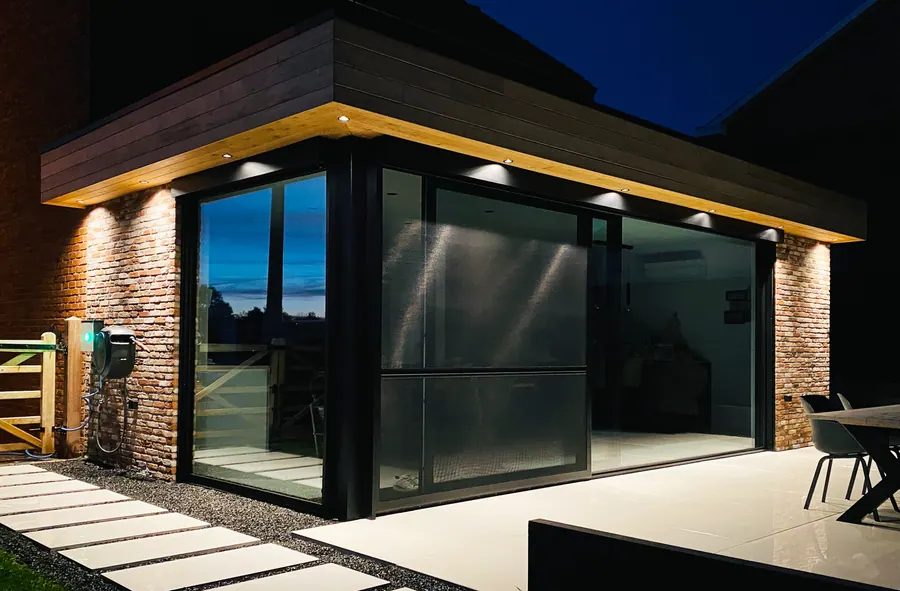 Aanbouw met grote glaspartij en cederhouten dakoversteek met LED-spots bij avondlicht